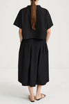 Person wearing a black top and skirt with a plain background rear view