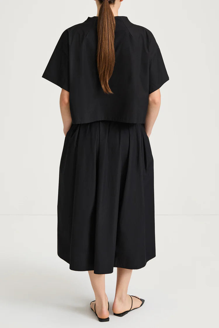 Person wearing a black top and skirt with a plain background rear view