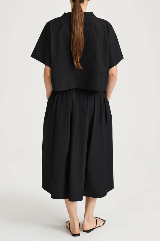 Person wearing a black top and skirt with a plain background rear view