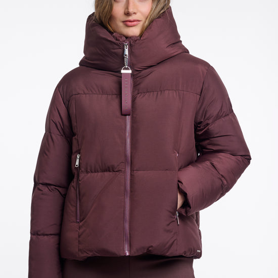 Woman wearing a maroon puffer jacket on a white background
