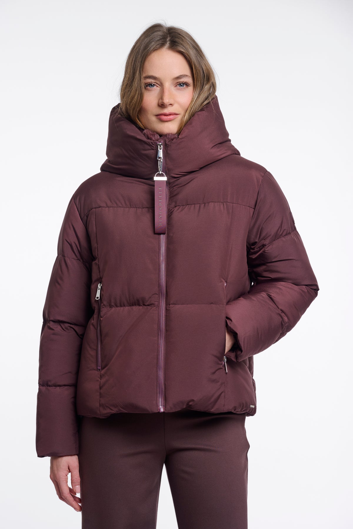 Woman wearing a maroon puffer jacket on a white background