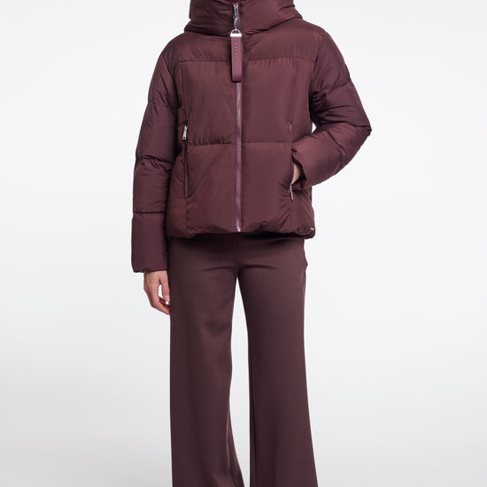 Woman wearing a maroon puffer jacket and pants on a white background