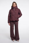 Woman wearing a maroon puffer jacket and pants on a white background