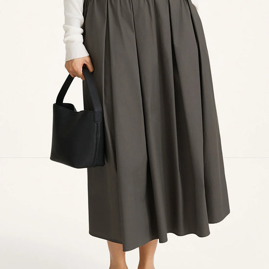Person wearing a gray skirt and white top, holding a black handbag on a white background
