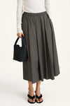 Person wearing a gray skirt and white top, holding a black handbag on a white background