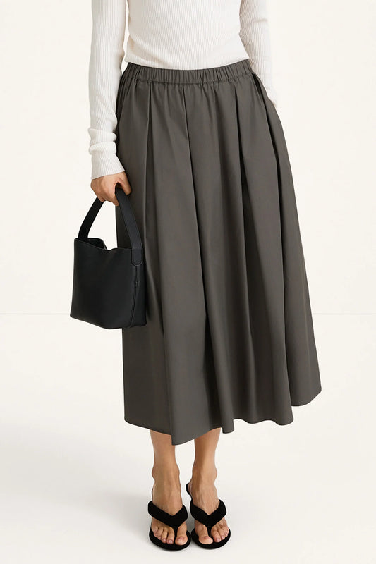 Person wearing a gray skirt and white top, holding a black handbag on a white background