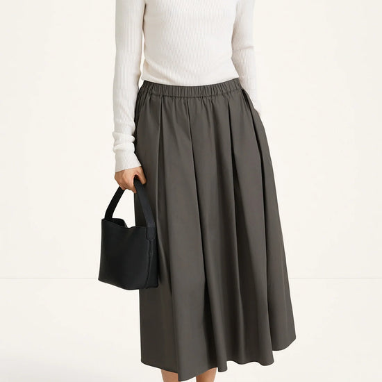 Person wearing a white turtleneck and gray skirt holding a black handbag on a white background