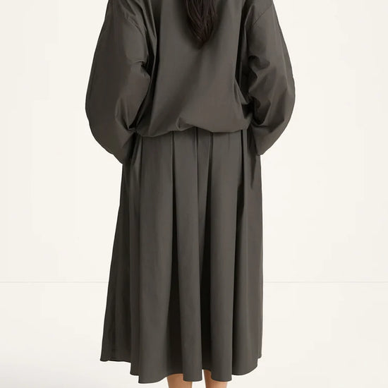 woman wearing a grey blouse and skirt on a white background rear view