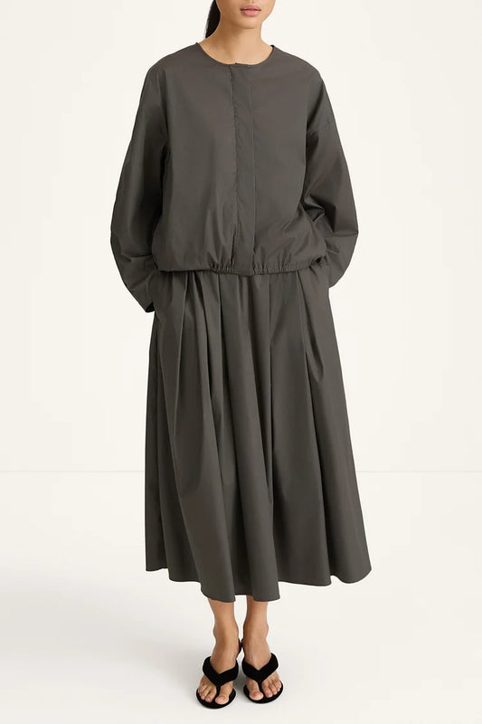 woman wearing a grey blouse and skirt and back heels on a white background 