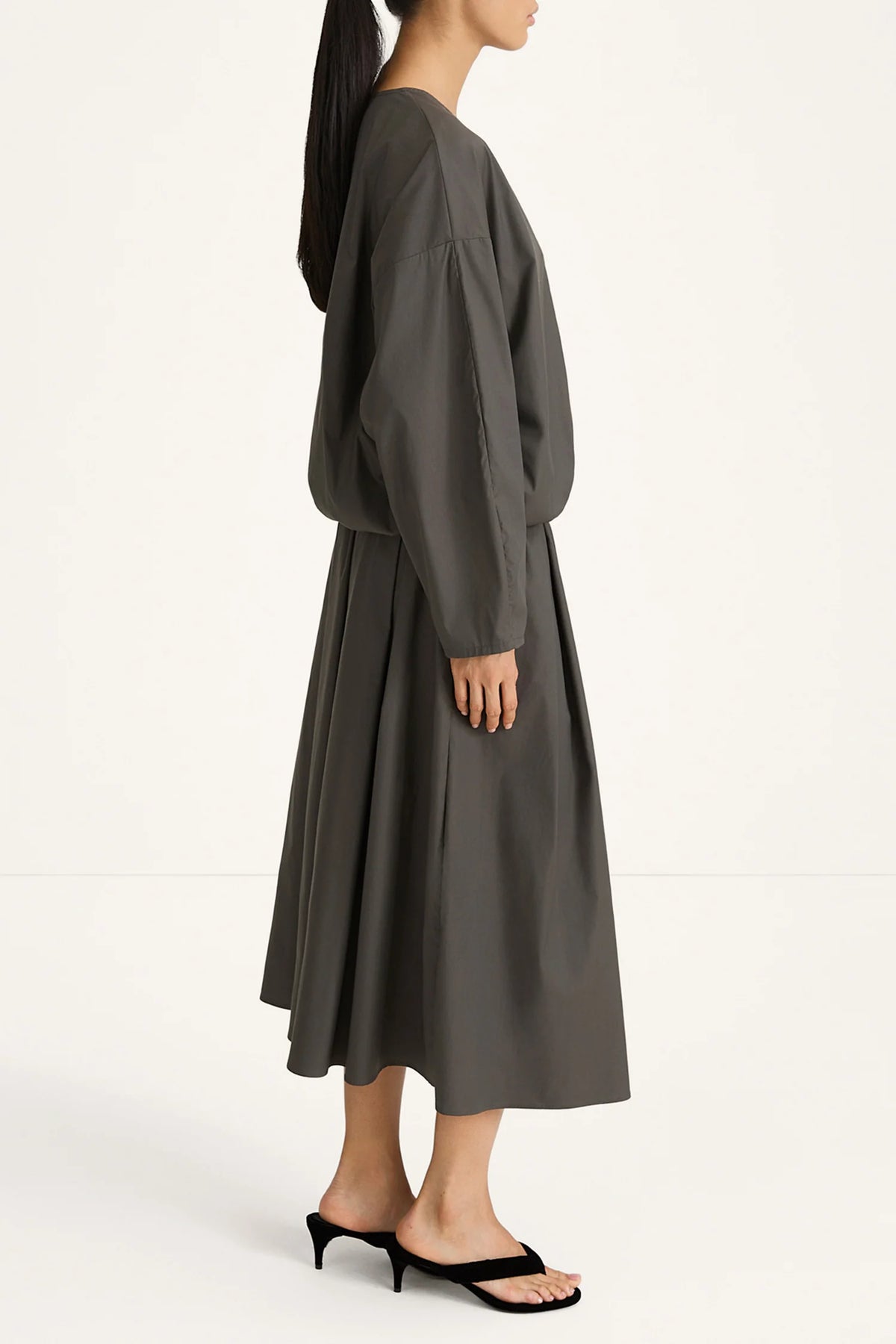 woman wearing a grey blouse and skirt on a white background side view