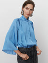 Light blue fluid fabric shirt with box pleats and raglan sleeves with high neckline and button through placket