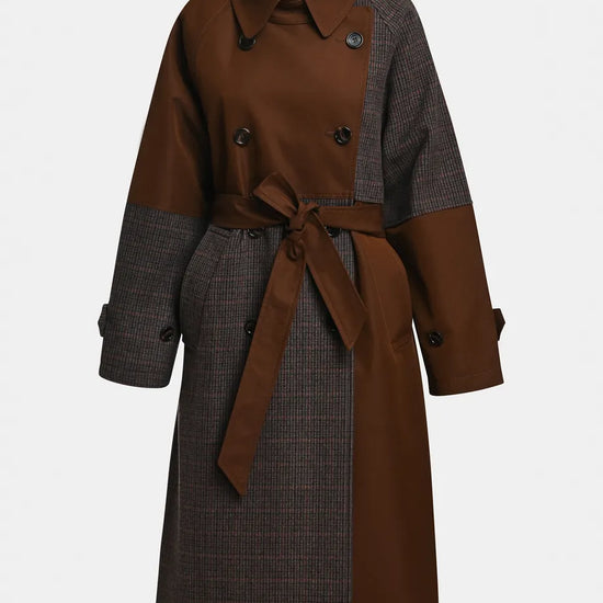 A double-breasted trench coat with a brown collar, double-breasted front, and a matching brown waist tie, featuring contrasting brown and dark gray patterned sleeves and side panels, shown on a light gray background.