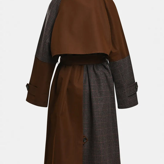 A color-blocked mid-length coat shown from the back, featuring a solid brown upper back and cape-like yoke, dark gray plaid sleeves, and a matching dark gray plaid skirt with a thin brown waist belt.