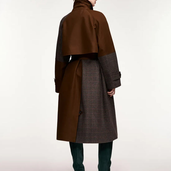 A model shown from the back wearing a long brown and dark gray coat with a high collar, dark green knee-high boots, and sunglasses, set against a plain light gray studio background.