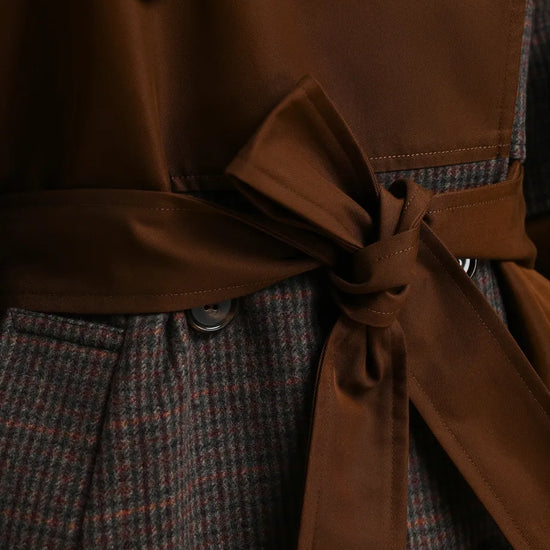 Close-up of a double-breasted coat with a brown satin-like waist tie and a brown-and-gray houndstooth patterned body, showing dark buttons.