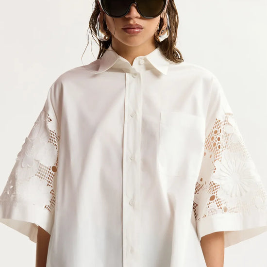 Woman wearing a white shirt with lace sleeves against a white background