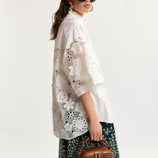 Woman wearing a white lace kimono-style garment with sunglasses and a brown bag on a white background
