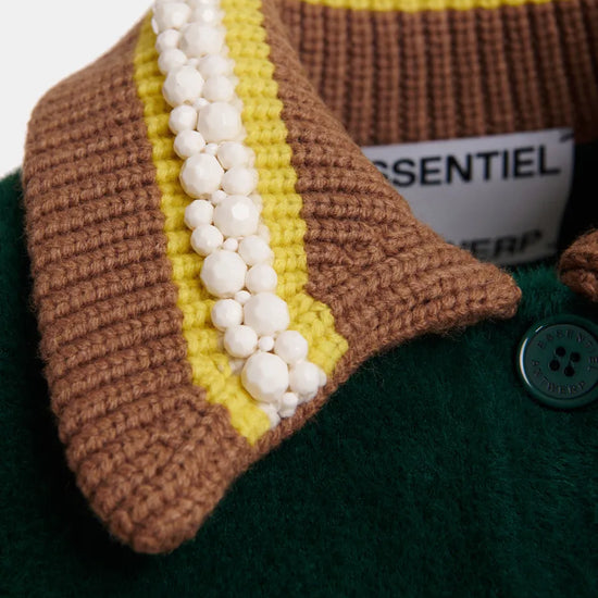 Close-up of a knit cardigan collar with brown and yellow stripes, white pom-pom trim, and a dark green wool body with a visible button.