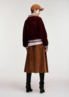 A model shown from the back wearing a dark burgundy fuzzy cropped cardigan over a striped shirt, a brown corduroy skirt, and black knee-high boots, against a plain light gray studio background.