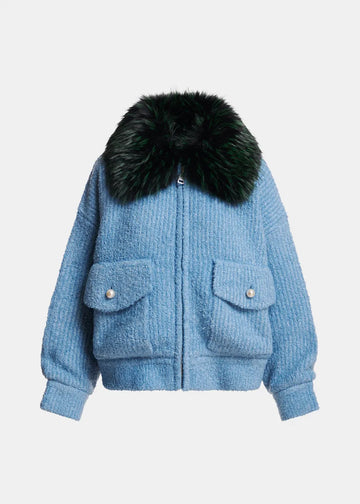 A light blue textured bouclé jacket with a large black fur collar, featuring two front flap pockets with silver-tone snap buttons, shown against a plain light gray background.