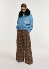 A model wearing a light blue textured jacket with a black fur collar, paired with wide-leg leopard print trousers, against a plain light gray studio background.