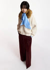 A model wearing a cream-colored knit zip-up jacket with a brown fur-trimmed collar, a light blue silk scarf, and dark burgundy wide-leg trousers, photographed against a plain white studio background.