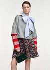 A model wearing a gray cropped sweatshirt with red and white striped sleeves, a blue and white striped bow tie scarf, a red and white floral mini skirt, and holding a dark green handbag against a light gray background.