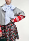 A model wearing a gray cropped sweatshirt with red and pink striped sleeves, a light blue and white striped bow tie, and a red, pink, and green floral skirt.