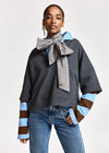 A model wearing a dark gray oversized sweatshirt with light blue and brown striped cuffs, a large checkered bow tie, and blue jeans, photographed against a light gray studio background.
