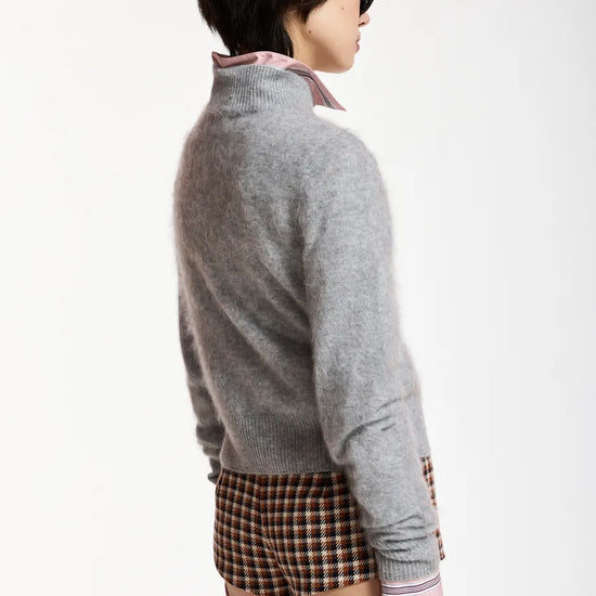 A model shown from the back wearing a light gray knit mock-neck sweater over a pink collared shirt, paired with brown and black plaid shorts, against a plain white background.