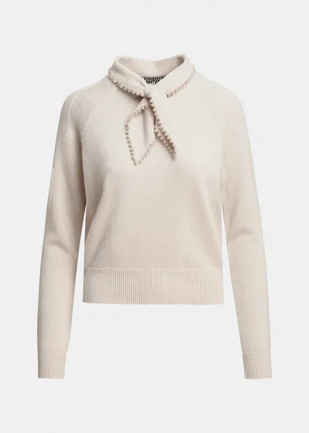 A cream-colored knit sweater with a high mock neck collar decorated with a beaded bow, shown on a plain light gray background.
