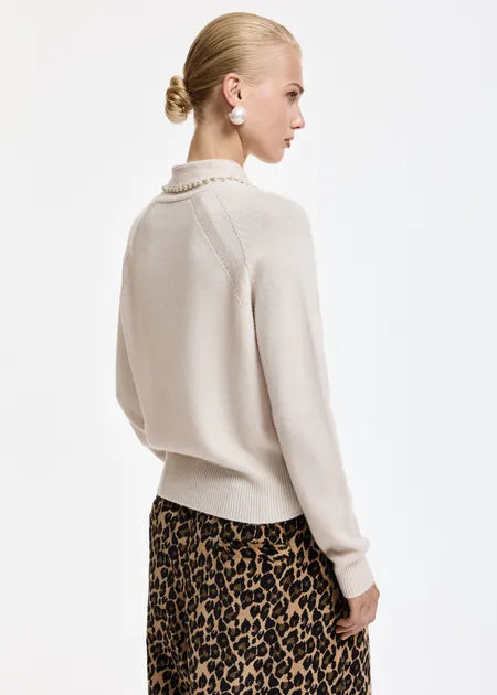 A model shown from the back wearing a cream-colored knit sweater with a pearl collar detail and a leopard print skirt, set against a plain white studio background.