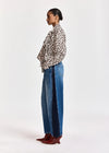 A model shown in profile wearing a leopard-print long-sleeve shirt, wide-leg blue jeans, and burgundy pointed-toe heeled boots against a plain white studio background.