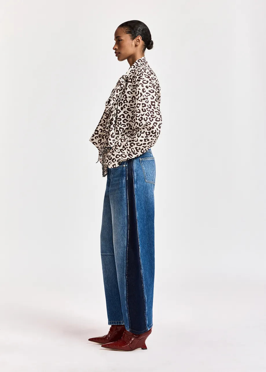 A model shown in profile wearing a leopard-print long-sleeve shirt, wide-leg blue jeans, and burgundy pointed-toe heeled boots against a plain white studio background.