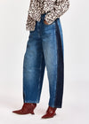 A person wearing wide-leg blue denim jeans with dark navy side panels, paired with a leopard-print top and red pointed-toe heeled boots, shown against a plain light gray studio background.