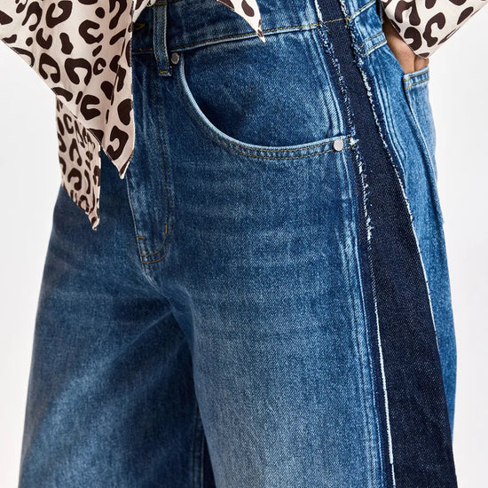 Close-up of a person wearing blue denim jeans with a dark side stripe and a leopard-print top partially visible at the top edge, against a plain light background.