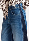 Close-up of a person wearing blue denim jeans with a dark side stripe and a leopard-print top partially visible at the top edge, against a plain light background.