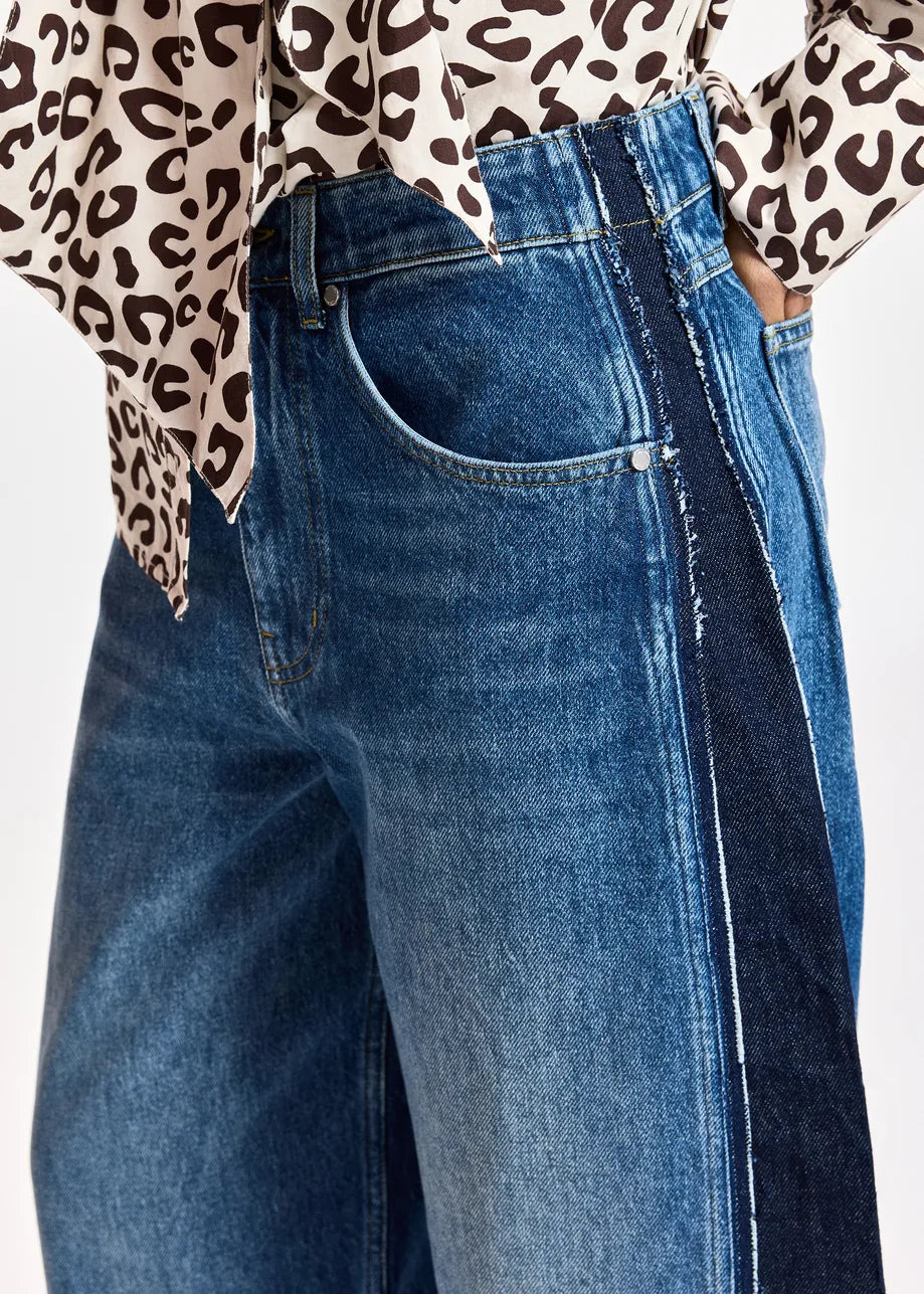 Close-up of a person wearing blue denim jeans with a dark side stripe and a leopard-print top partially visible at the top edge, against a plain light background.