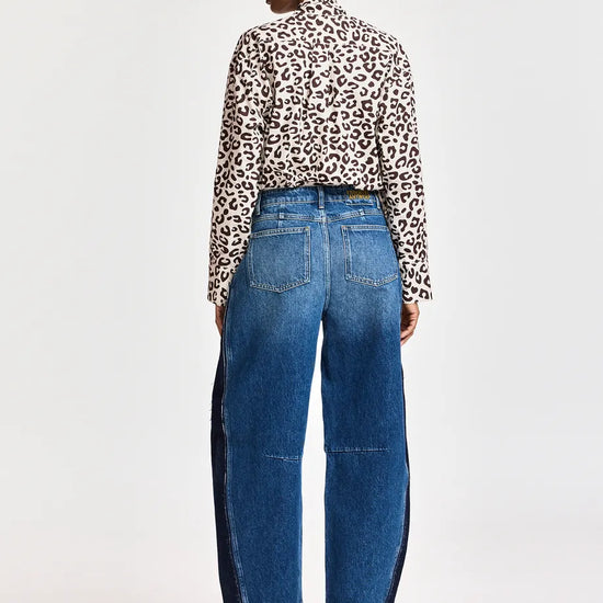 A model shown from the back wearing a leopard-print long-sleeve shirt, blue wide-leg jeans with dark side panels, and brown pointed-toe boots, against a plain light gray studio background.