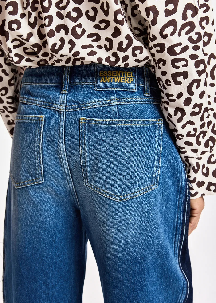 Close-up back view of a person wearing blue denim jeans with a leopard-print long-sleeve top. The waistband shows a gold-tone patch reading 'ESSENTIELS ANTWERP'.