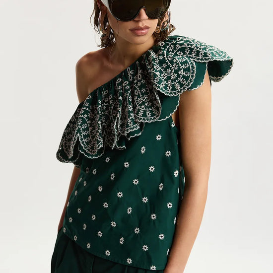 Woman wearing a green one-shoulder top with floral pattern and sunglasses on a white background
