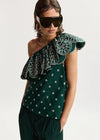 Woman wearing a green one-shoulder top with floral pattern and sunglasses on a white background