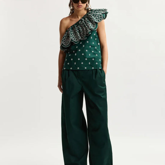 Woman wearing a green one-shoulder top with ruffled details and matching pants on a white background