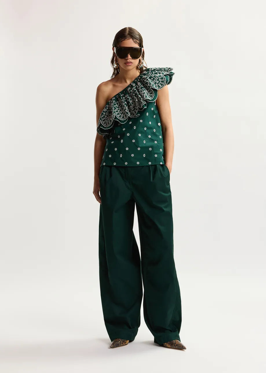 Woman wearing a green one-shoulder top with ruffled details and matching pants on a white background