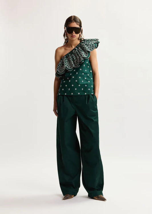 Woman wearing a green one-shoulder top with ruffled details and matching pants on a white background