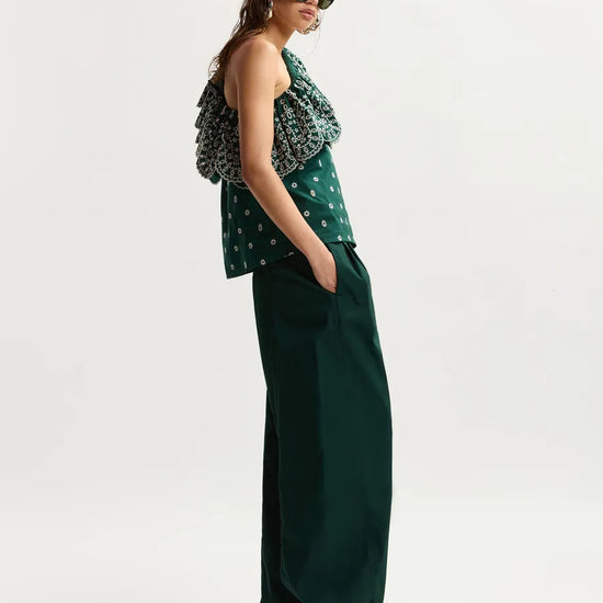 Woman wearing a green patterned top and dark green wide-leg pants on a white background