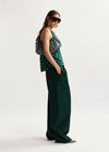 Woman wearing a green patterned top and dark green wide-leg pants on a white background