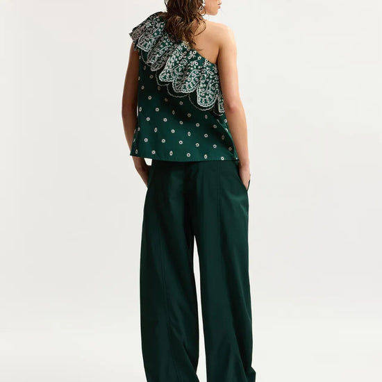 Woman wearing a green one-shoulder top and wide-leg pants on a white background