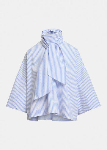 A light blue and white striped blouse with a high gathered mock neck, a large front bow, and wide draped sleeves, shown against a plain light gray background.