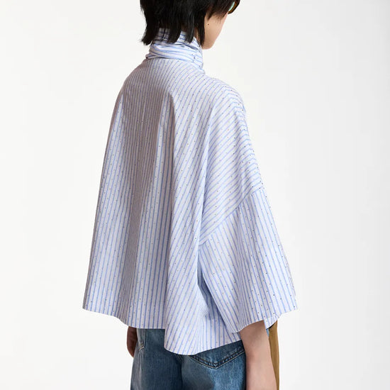 A model shown from the back wearing a light blue and white vertically striped high-neck shirt with wide three-quarter sleeves, paired with blue jeans, against a plain white background.